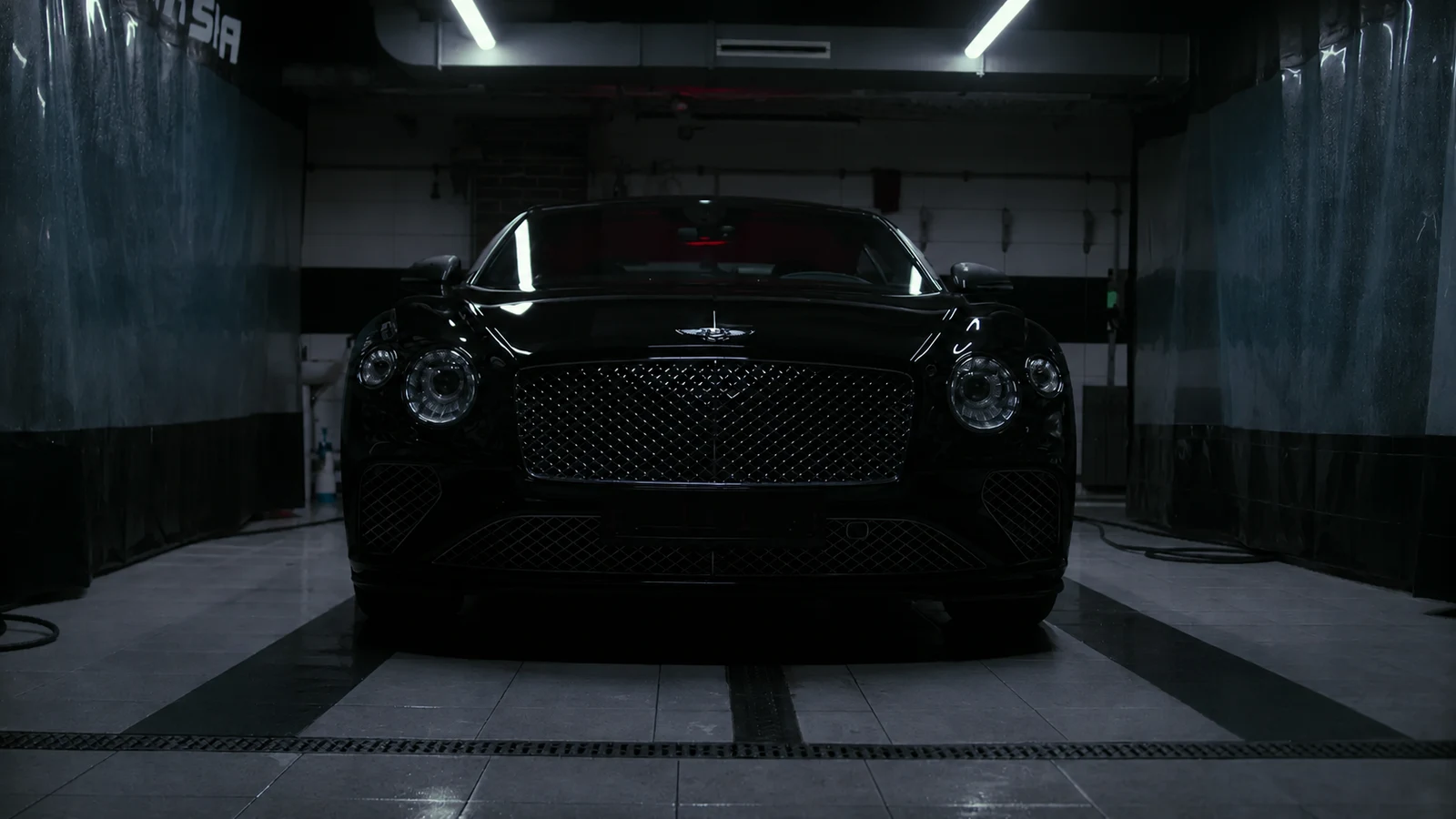 A black luxury car with its headlights off in a dim studio